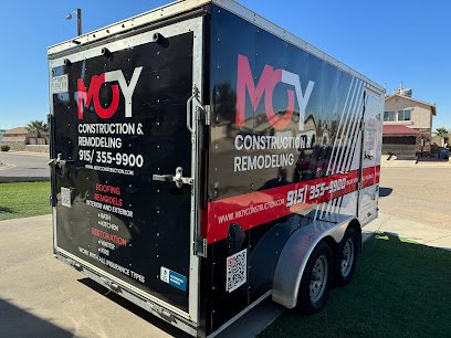 A black enclosed trailer parked on a lawn in a suburban neighborhood, branded with the Moy Construction & Remodeling logo, phone number (915‑355‑9900), list of services (roofing, remodels, restoration), the website URL, and a QR code.